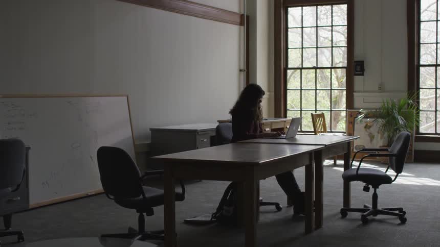 A long haired woman in eyeglasses sitting at a laptop while typing on a laptop