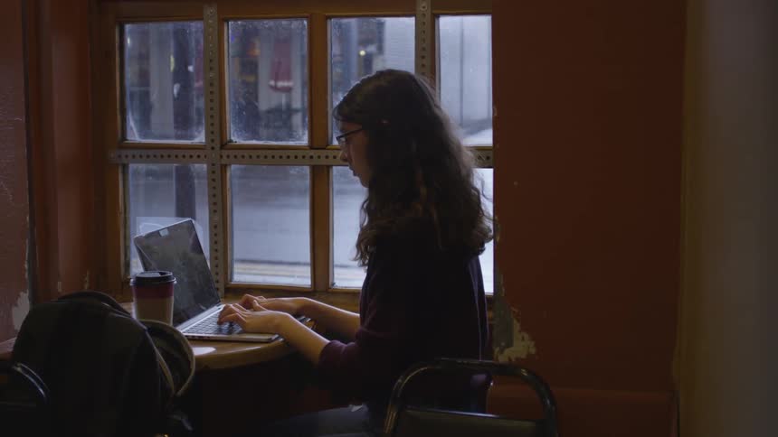 A woman is sitting down and typing on a laptop