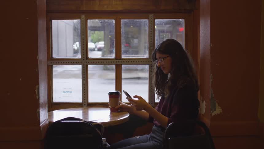 Woman texts on phone while sitting with a cup of coffee