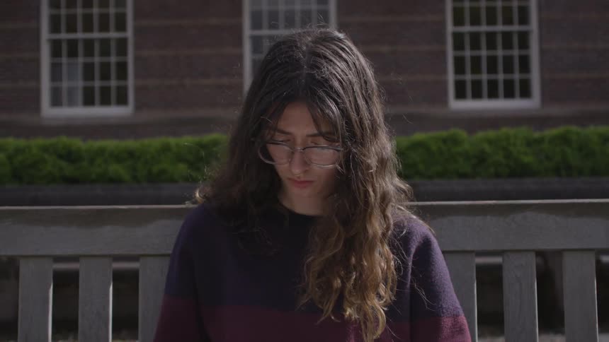 A woman is sitting outside while looking down
