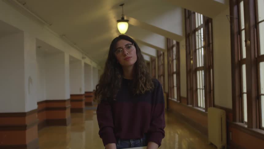 Woman stands in empty hallway holding book