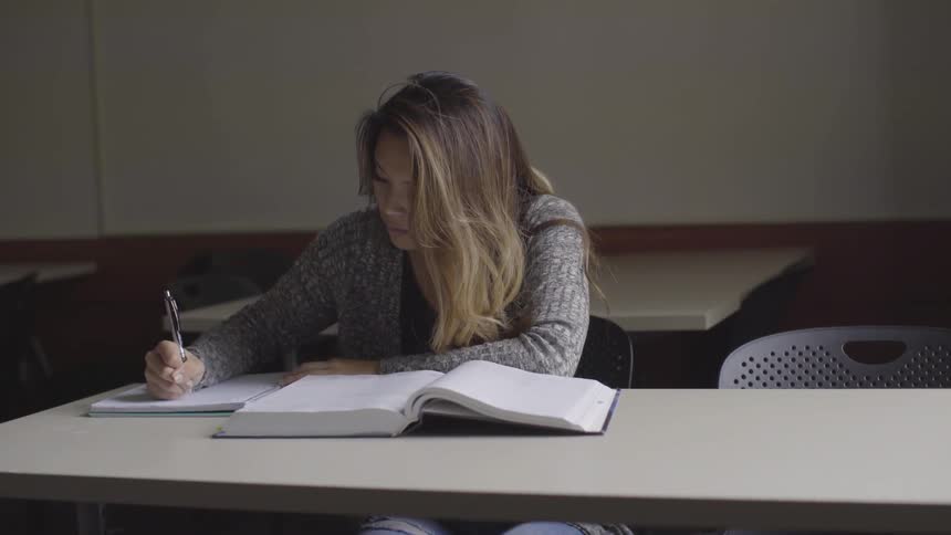 Woman makes notes in notebook while reading textbook