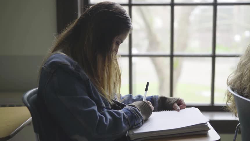 A young female sits and her desk by a Georgian window and writes in notepad