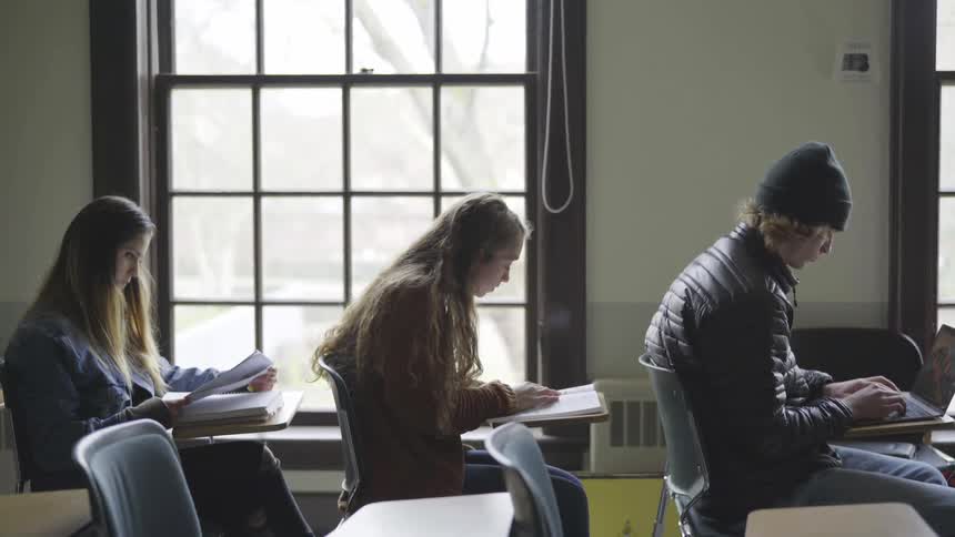 Three students sit at desks reading and working
