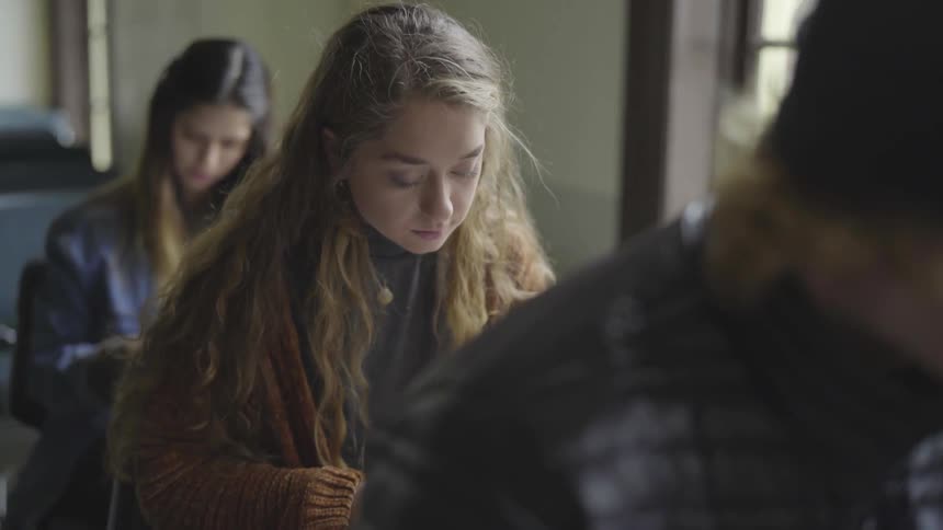 Male and female teenage students sit in a classroom looking down at their desks and reading