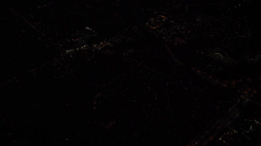 The camera flies over a dimly lit city at night