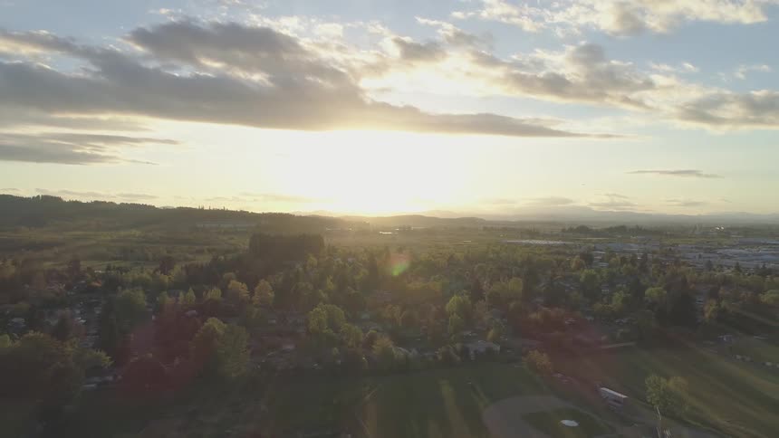 Camera flies over a town with the sun rising in front of it