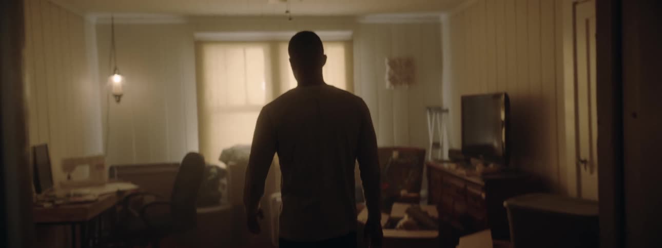 Man walks into dim room and holds head