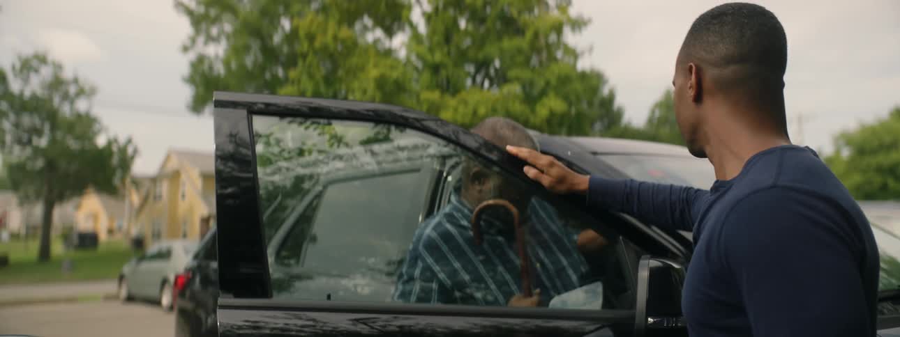 Man helps an elderly person into a car