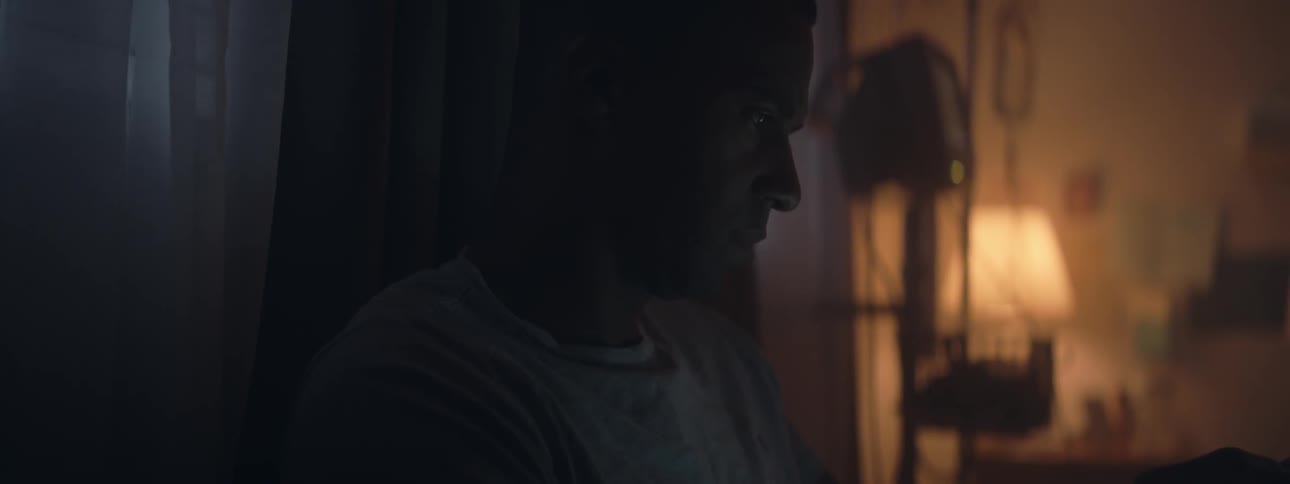 A man swipes and taps on a cell phone in a dimly lit room