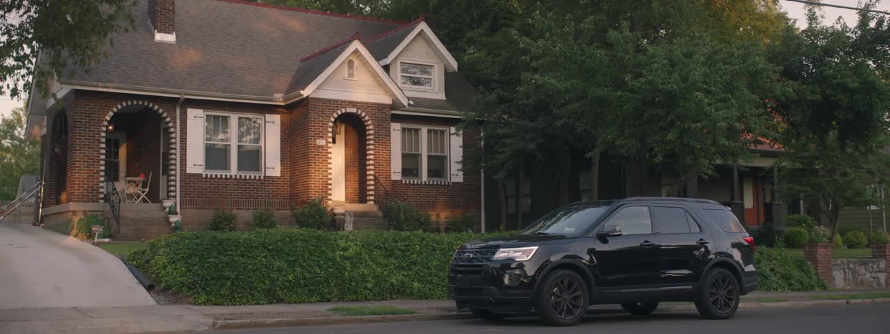 A black car parks in front of a house and a man gets out