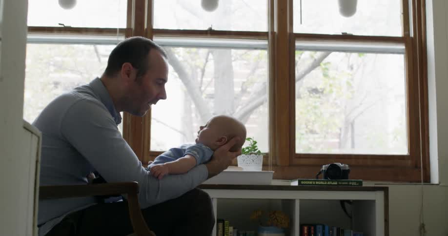 A man is holding a baby by a window