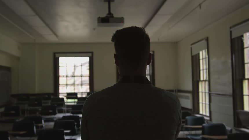 A man is standing in an empty classroom