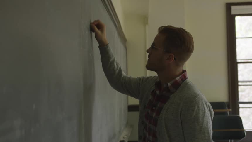 A teacher writes out a lesson on the chalkboard during class
