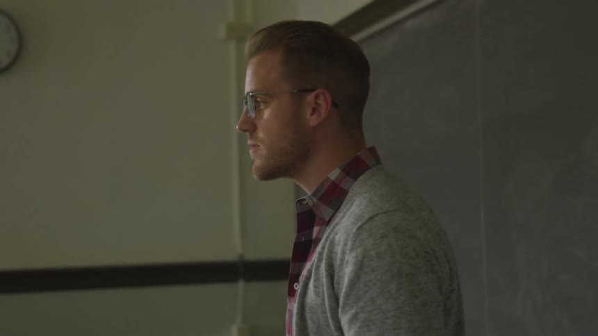 A blonde man with spectacles delivers a talk in front of a blackboard