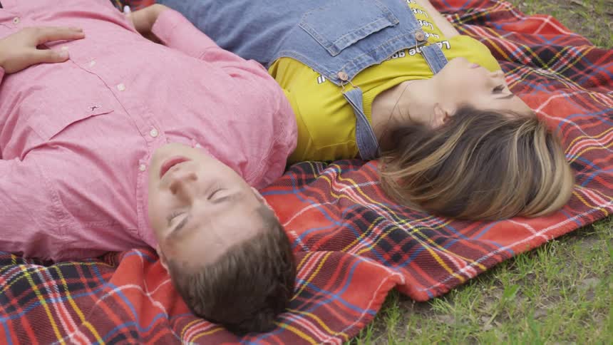 Woman and man lying down on the grass look at each other then turn their heads by day