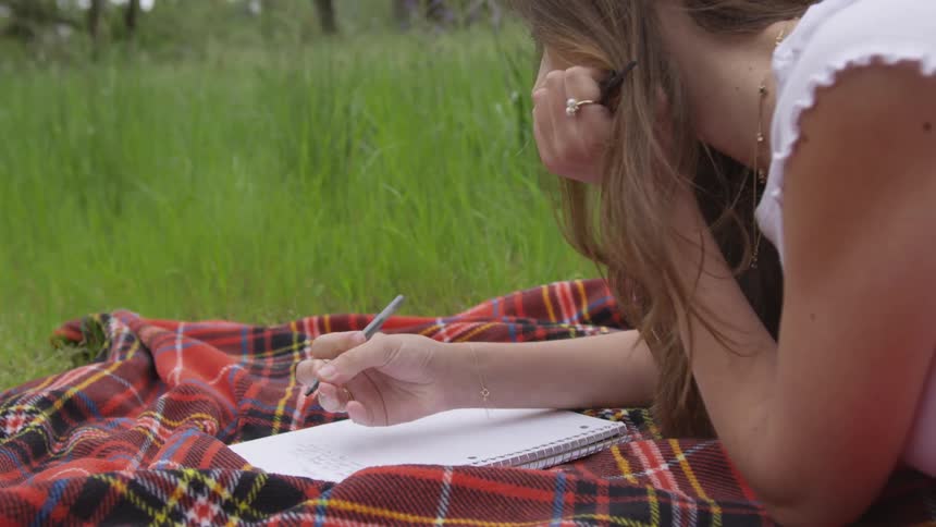 Woman writing on a notebook on a blanket over the grass