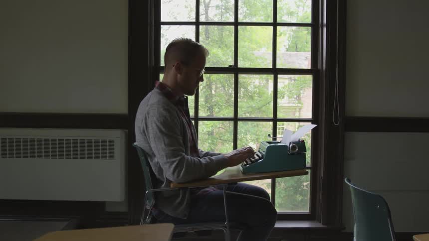 Man sits at desk in classroom and uses typewriter