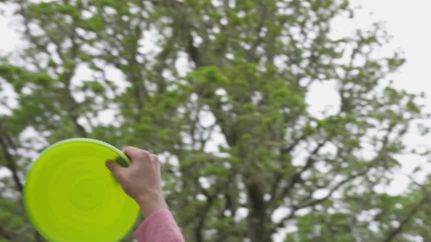 A green frisbee flying and being caught by someone