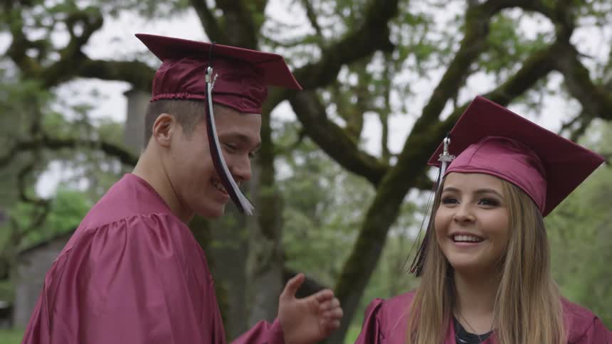 A woman putting a cap on a man while they are both in graduation outfits
