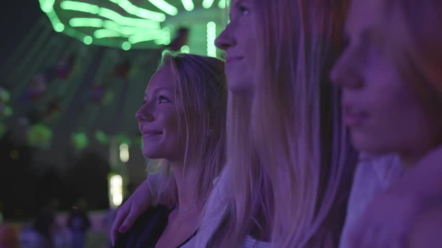 Female friends hug and look at lights at a carnival