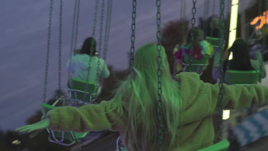 Blonde caucasian teenager rides on an amusement park ride at dusk