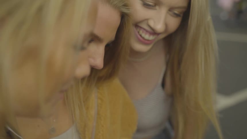 Three blonde women look at something and smile