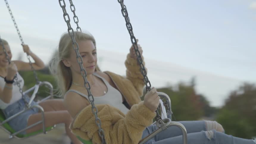 Two blonde girls swing in theme park by day