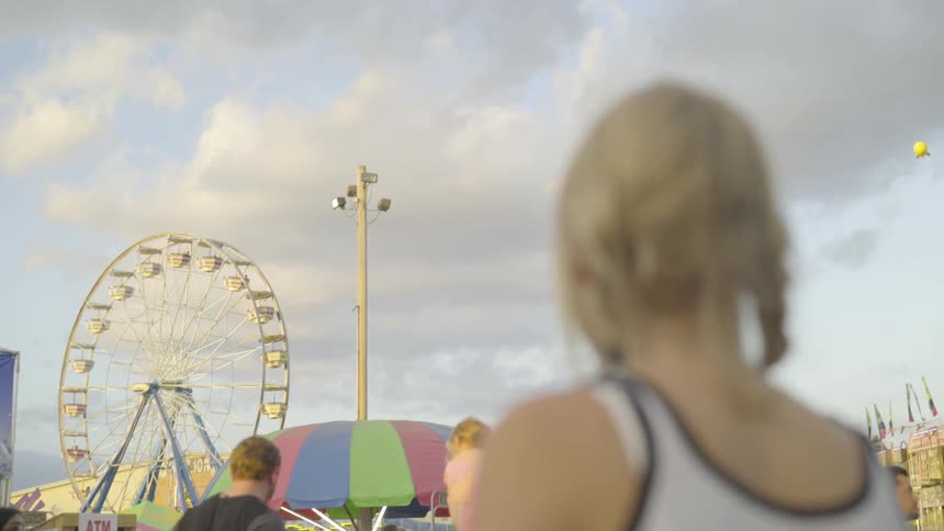 Teenage girl looking at a ferris wheel in the distance at a carnival
