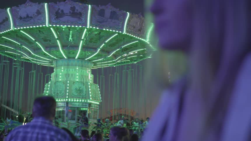 People walk around carnival at night with woman in foreground