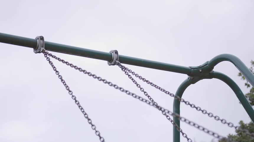 A swing set goes back and forth with only the chains visible
