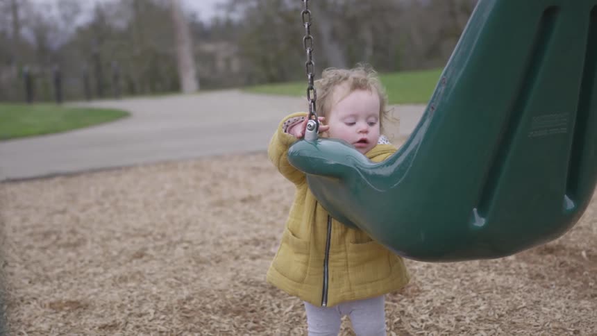 Toddler standing at a swing at the playground