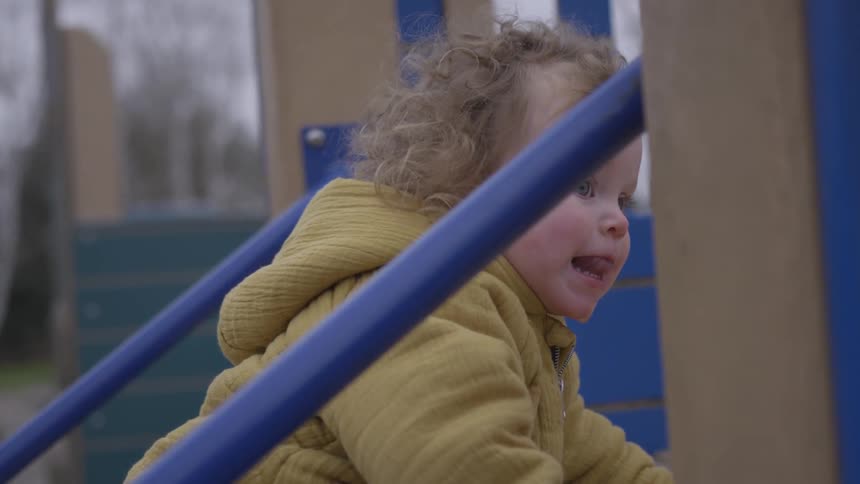 Toddler girl climbs on playground equipment