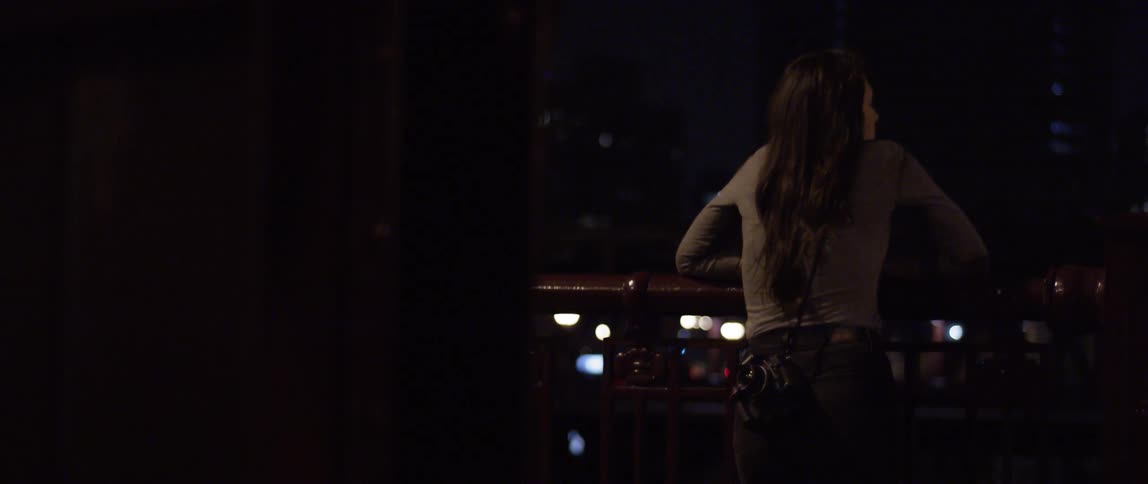 A woman leaning over a rail and overlooking a city at night