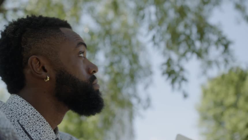 Black man contemplating a tower while sitting at the park