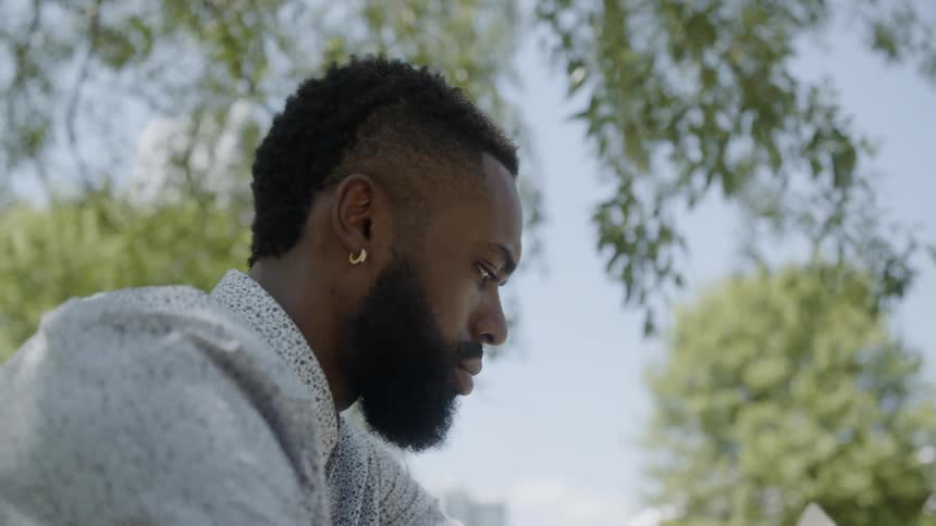 A young black man sits outside reading