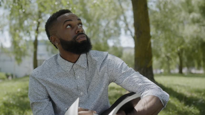 Black man sitting in park surrounded by trees