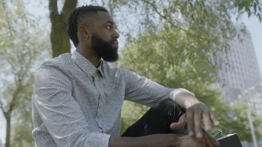 Black man sitting in park under a tree writing
