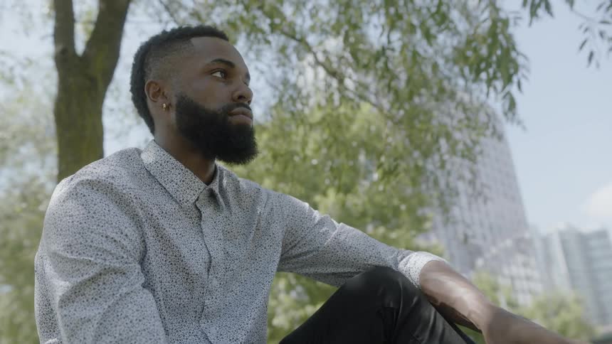 Black man writing in book before closing and hitting it on his hand before looking around
