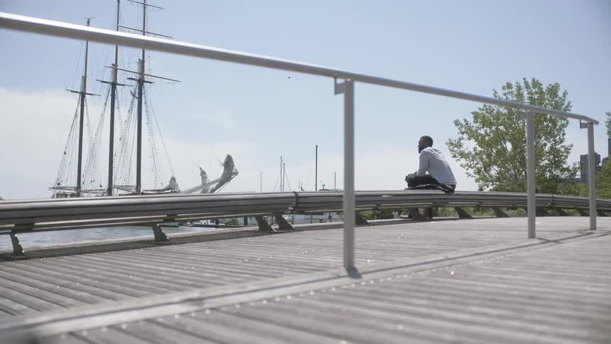 Man sits at harbor looking towards ship