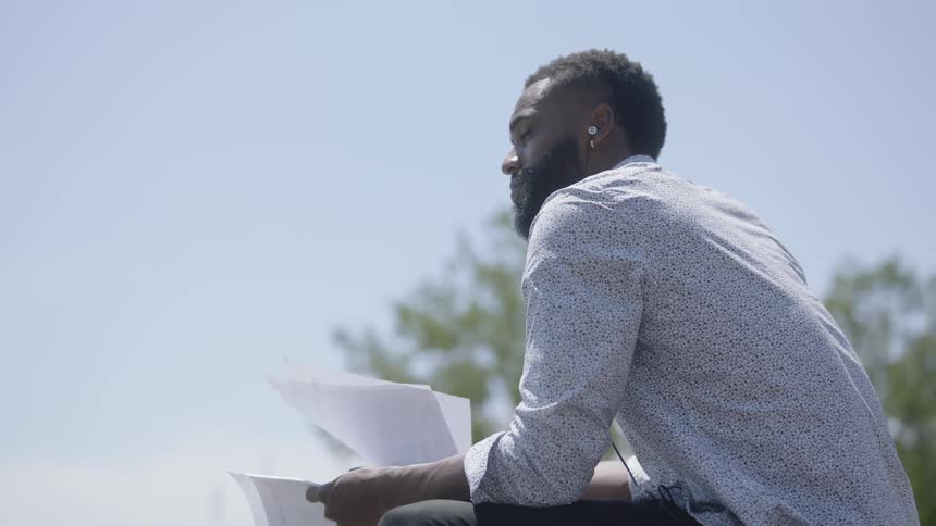 A man with earbuds in his ears looks at papers he is holding and looks into the distance