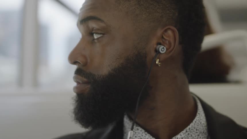 A man wearing earbuds sits on a bus