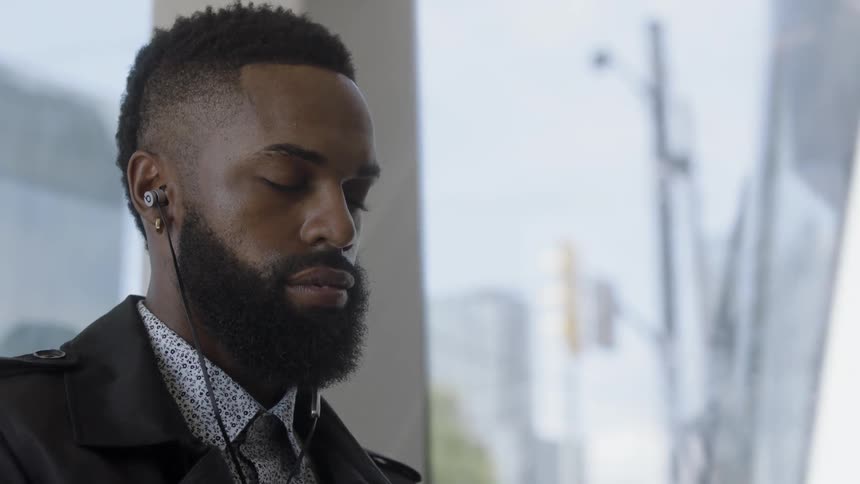 A bearded black man listens to music on a cloudy day