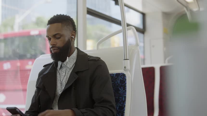 Man adjusts his earbuds as he holds his cell phone