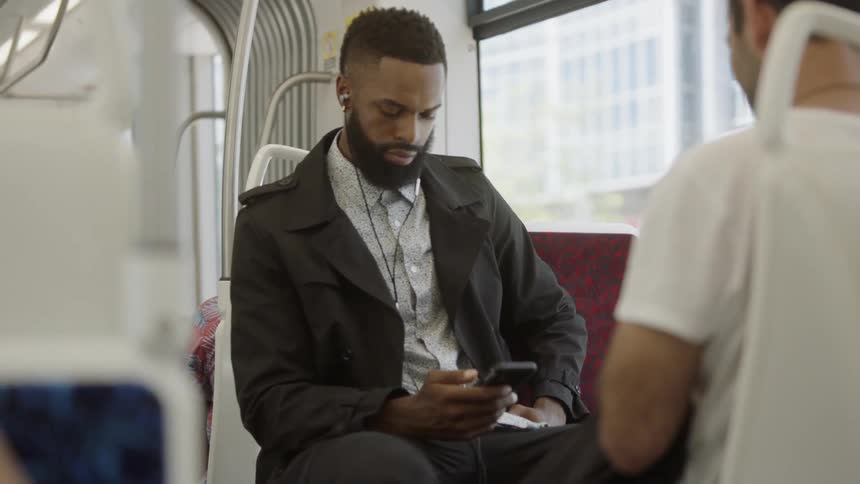A man sits on an elevated train looking at his phone