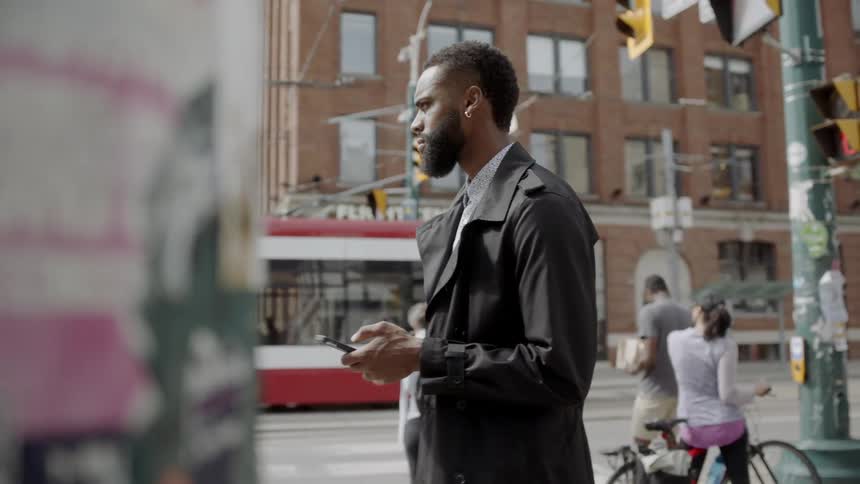 A man typing on his phone in a busy city street while a trolley drives past