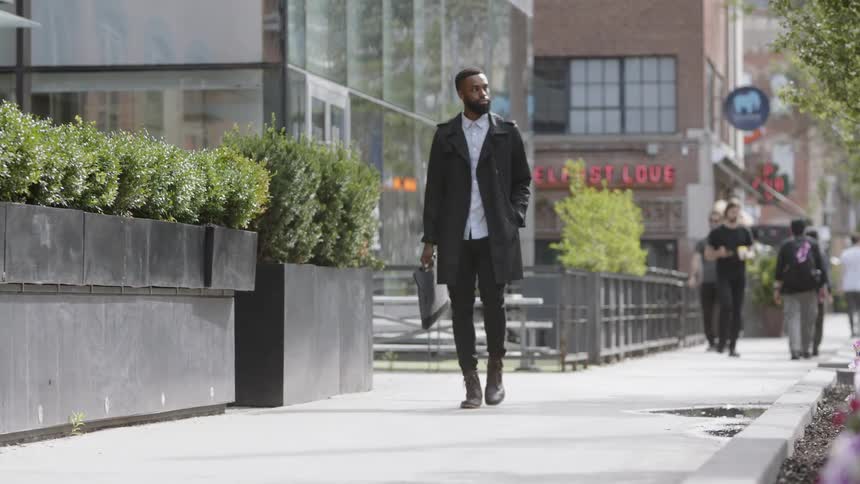 A young black man walks down a city sidewalk