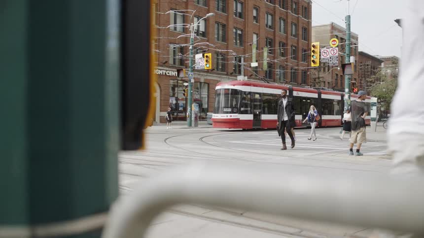 Pedestrians cross a city street while a passenger train drives by