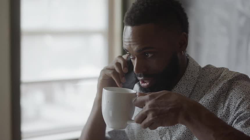 A man talks on a cell phone while drinking from a mug
