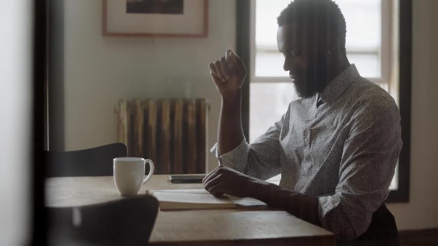 A man sits at a table and reads a book